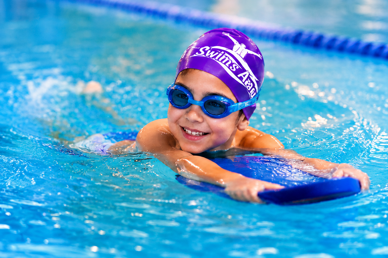 Child smiling in the pool wearing Swims Away swim cap and goggles